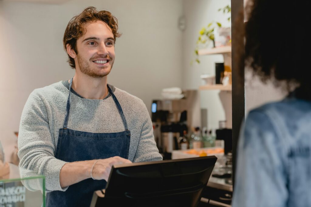 Smiling helpful young waiter servicing the customer at cash point in cafe